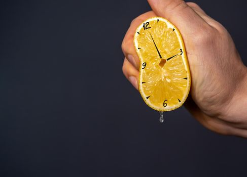 Hand squeezes out a lemon, on which the clock is drawn. Creative hours as a symbol of wasted time, overwork and poor planning. Nutritious citrus as benefits, a person's contribution to their health.