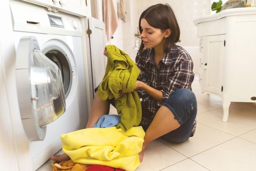 A young girl puts things in the washing machine, a woman sits on the floor of a cozy house and looks at the stain on her jacket, which needs to be removed with detergent.