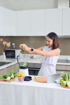 Healthy Asian woman enjoy making green vegetables detox cleanse and green fruit smoothie with blender in kitchen at home. dieting concept.healthy lifestyle