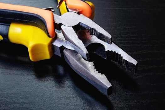 Two pliers, tools on a black wooden table close up