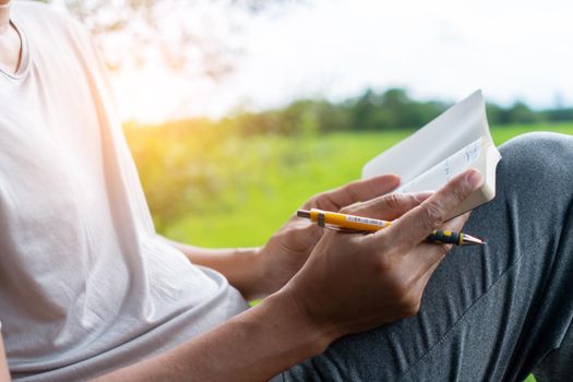 In a public park, a man is handwriting in a small white memo pad to make a note of something he doesn't want to forget or to make a to-do list for the future concept.