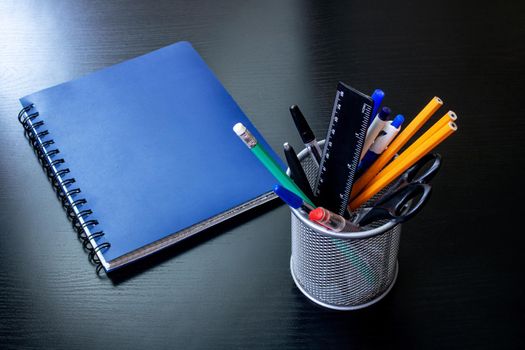 Stand with office supplies and a blue notebook on a black wooden table