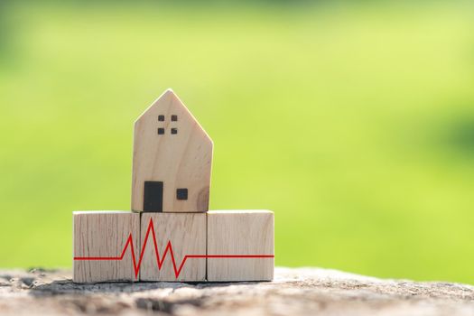 The concept of a crisis situation time financial difficulty is represented by a wooden cube with a house model and a heart pulse indication.