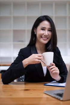 Portrait of cheerful asian woman looking camera and tablet on desk in office. Concept of young business people.