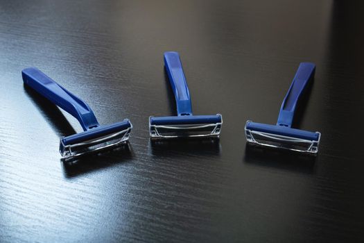 Three blue razors on a wooden background close up