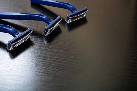 Three blue razors on a wooden background, copy space