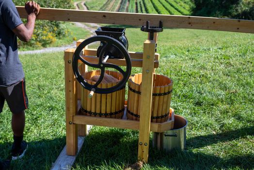 Beautiful cider press on a hillside with a farm in the background. Young African Americna man turns the crank on the press. Shot in natural light with copy space.