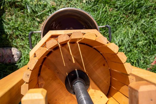 Beautiful wooden press and heavy metal plunger seen from above with pan underneath catching cider that runs out. Bright green grass background, sunshine, natural light and copy space. No people.
