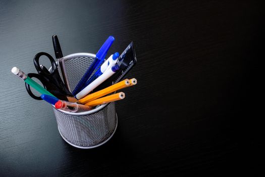 Metal stand with pencils, pens, scissors on a black wooden table close up