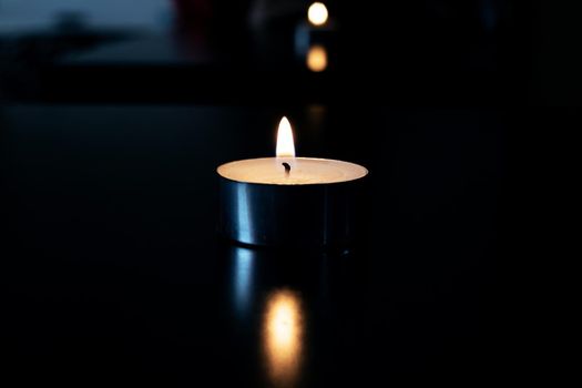 Flame of a small candle in the dark with reflection