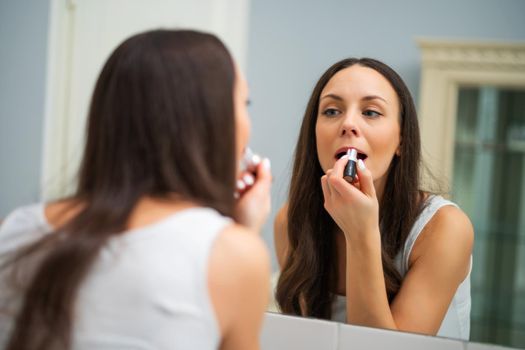 Young woman is applying lipstick in the bathroom.