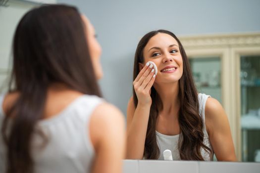 Portrait of young woman who is cleaning skin on her face.