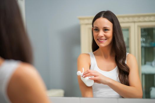 Portrait of young woman who is applying skin cream.