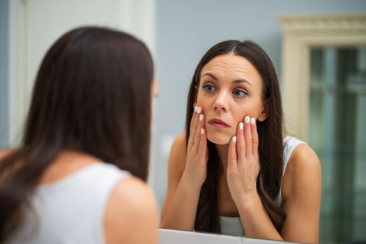 Tired woman looking at her eye bags in the bathroom.