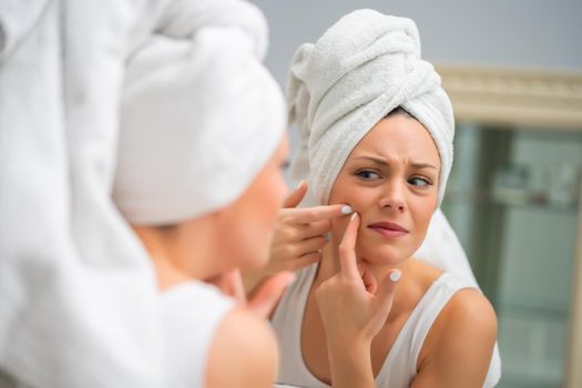 Young woman is squeezing pimple in the bathroom.