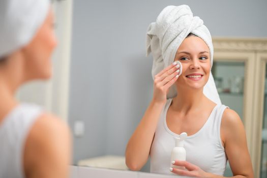 Portrait of young woman who is cleaning skin on her face.