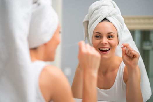 Young woman is using dental floss to clean her teeth.