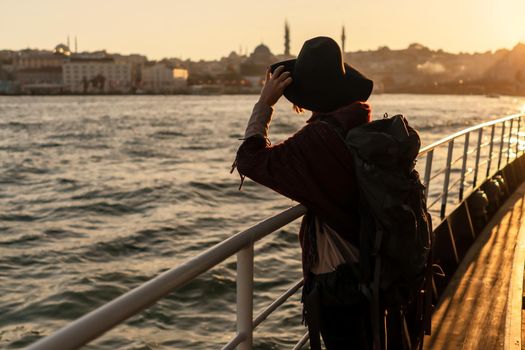 A young girl in a hat and with a backpack looks at the coast of Istanbul from the side of the ferry. The beginning of a great adventure in the Arab countries.