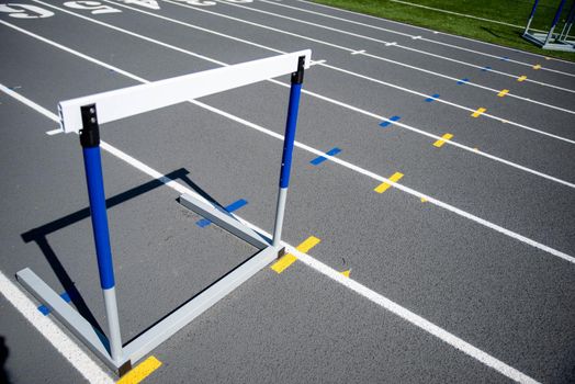 A lone hurdle sits on a gray running track with fresh crisp white lines. No people, shot in natural light with copy space.
