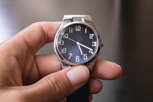 Blue wristwatch in hand on gray background close up