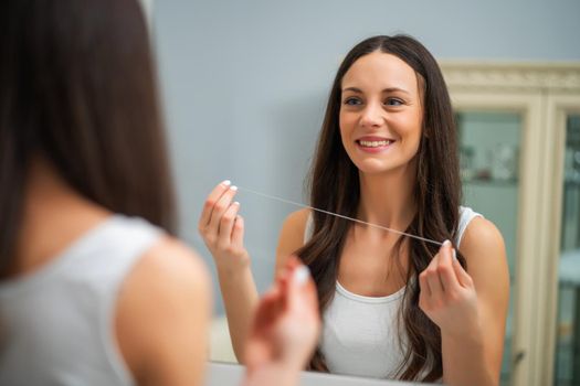 Young woman is using dental floss to clean her teeth.