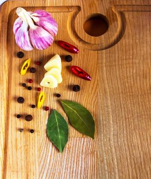 A whole head and a clove of garlic, cut into slices, hot red and yellow peppers, cut into rings, a bay leaf and a mixture of peas are on a wooden cutting board. Vertical photo, copy space. High quality photo