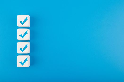 Four blue checkmarks on white cubes in a row against blue background with copy space. Concept of questionary, checklist, to do list, planning, business or verification. Modern elegant flat lay