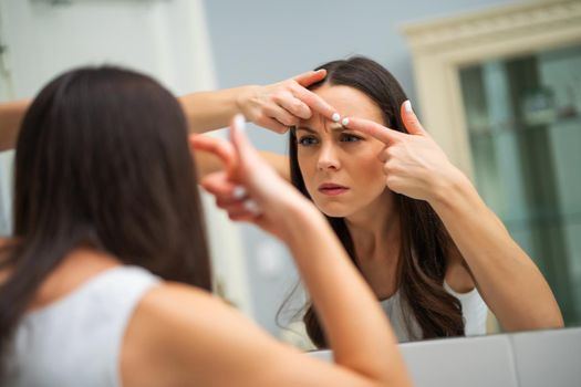 Young woman is squeezing pimple in the bathroom.