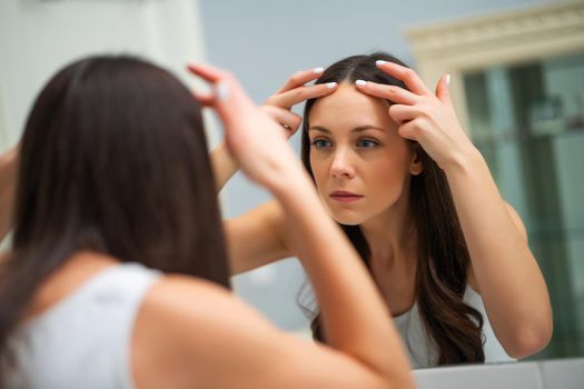 Worried woman is looking at her wrinkles in the bathroom.