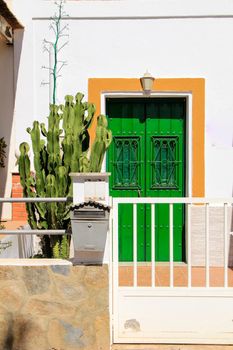 Wooden door painted green with metal details. White fence, mailbox and cactus pots at the door.