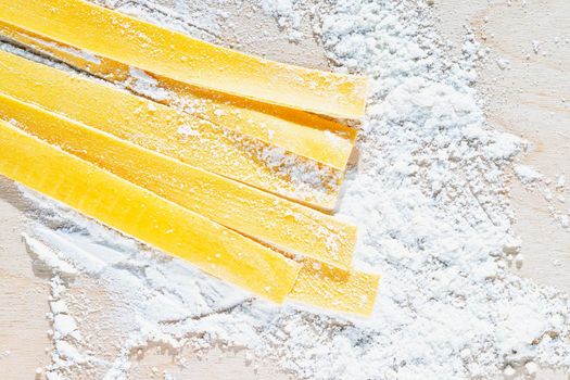 Large flat egg  pasta pappardelle with flour on wooden background , uncooked pasta