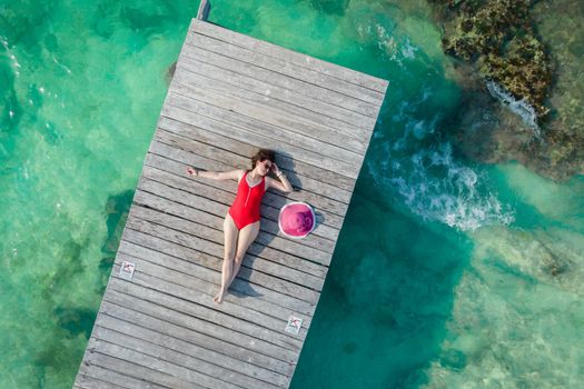 Aerial view of woman on wooden pier at sunny summer day in Cancun, Mexico, top view. Young sexy woman in red swimsuit in summertime in Caribbean. Summer beach vacation concept