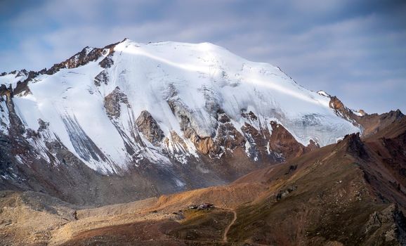 Rocks of the highlands, the road among the snow-capped peaks of the mighty mountains in the sun.