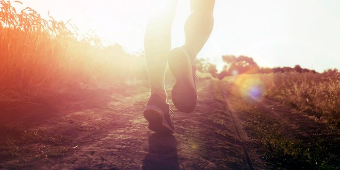 Athlete runner legs running on a close-up of a trail across a field on a shoe. Fitness and warm-up, young man with sun effect in the background and open space around him.