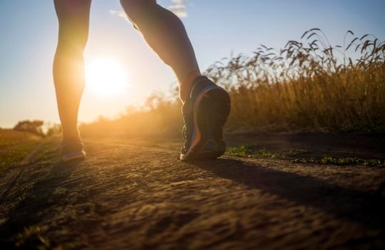 Athlete runner legs running on a close-up of a trail across a field on a shoe. Fitness and warm-up, young man with sun effect in the background and open space around him.