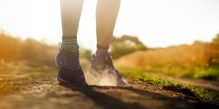 Female athletic legs in sneakers at sunset during outdoor jogging at sunset. A young girl warms up, she is engaged in trail running, view on her legs and clouds of dust close-up.