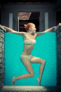 Attractive slim red woman in blue swimming pool with transparent wall