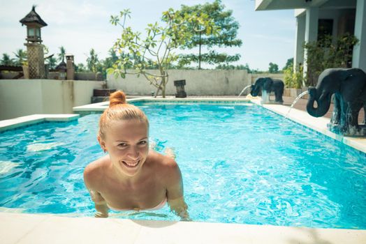 Young woman wearing swimsuit relaxing near swimming pool at exotic location