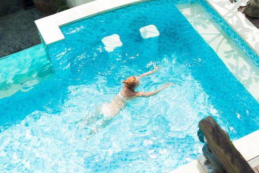 Young woman wearing swimsuit relaxing near swimming pool at exotic location