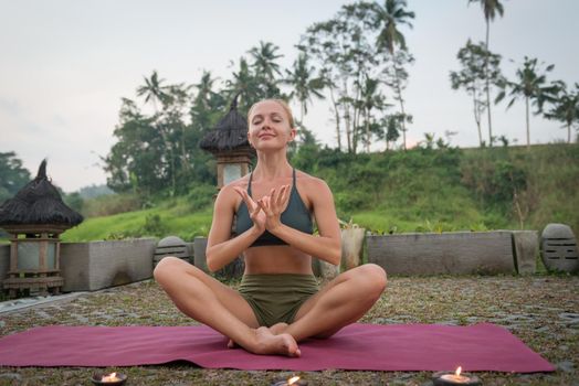Young woman meditating in lotus posture at sunset with candles