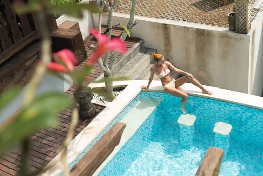 Young woman wearing swimsuit relaxing near swimming pool at exotic location