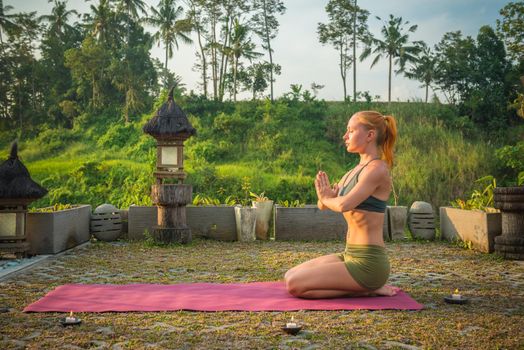 Young woman meditating in lotus posture at sunset with candles