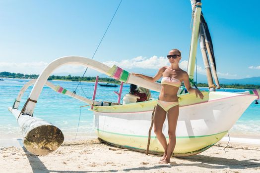 Slim young woman posing with boat at tropical beach