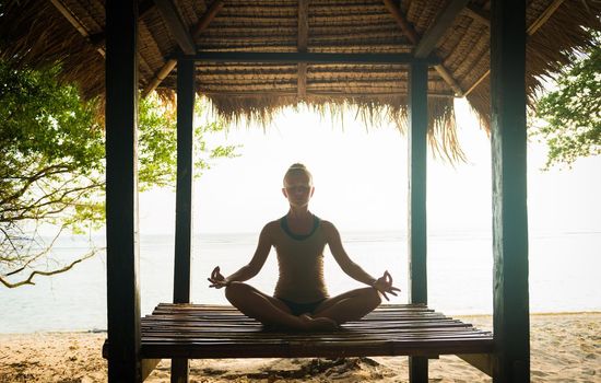 Young woman meditating in lotus pose at the ocean shore