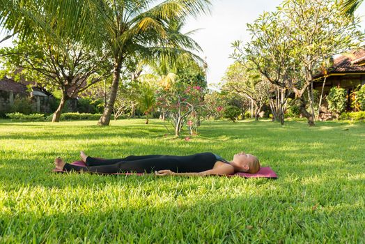Shavasana. Young woman doing yoga exercises in the lush tropical garden