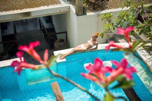 Young woman wearing swimsuit relaxing near swimming pool at exotic location