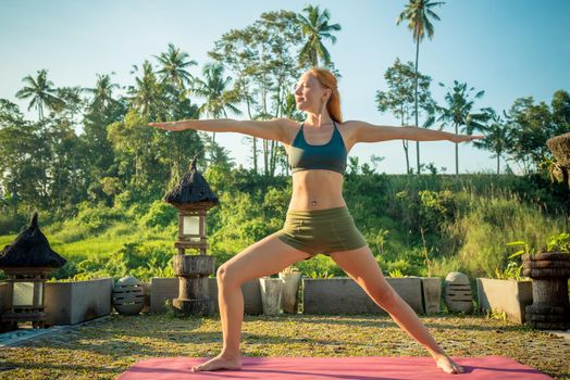 Young woman performing yoga asana at sunset with jungle background