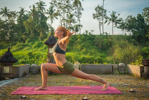 Young woman performing yoga asana at sunset with candles