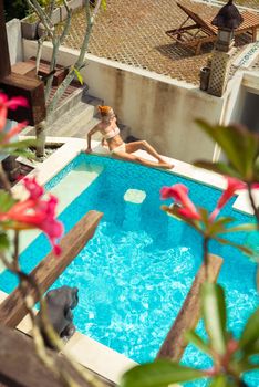 Young woman wearing swimsuit relaxing near swimming pool at exotic location