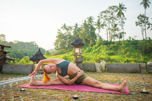 Young woman performing yoga asana at sunset with candles